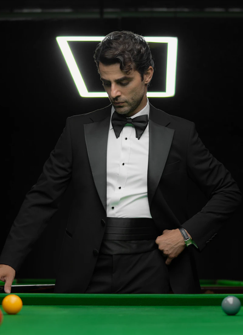 Man wearing an elegant black tuxedo at a billiards table